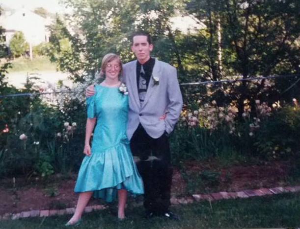 Two teens posed before prom, a girl in a mint green satin dress next to a boy in a Depeche Mode-esque grey and black suit.
