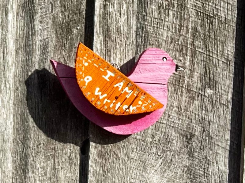 A wooden bird with "I am a writer" painted on its wing.